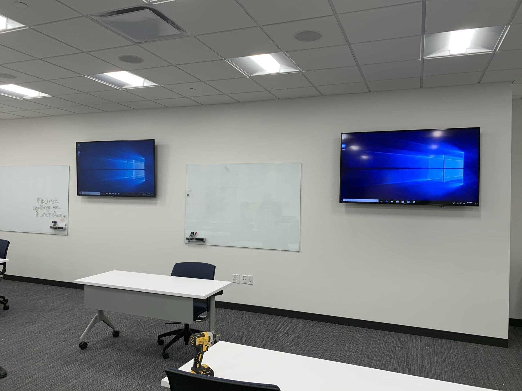 Dual wall-mounted displays flanking glass whiteboards in a Dallas office training room