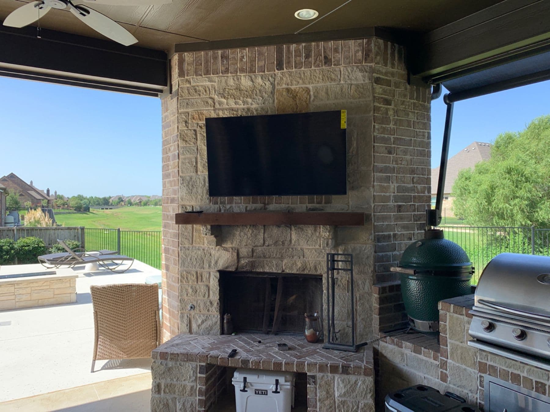 Outdoor TV mounted above a stone fireplace overlooking a golf course — Cognito Media Services install, Southlake TX