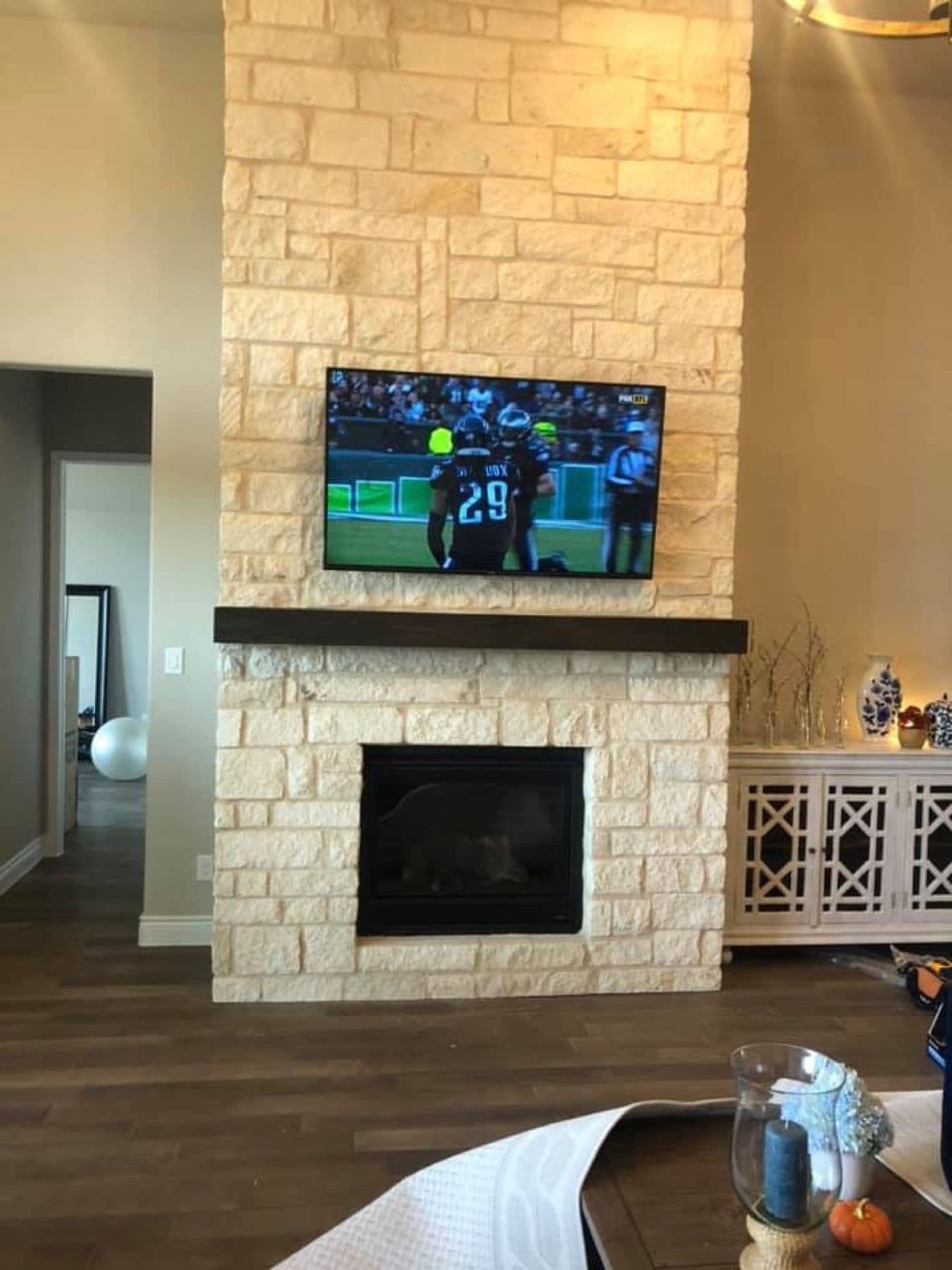 TV mounted over a stacked-stone fireplace with a wood mantel, wires concealed, Cognito Media Services install, Highland Park TX
